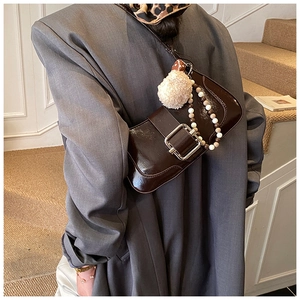 Detailed view of dark brown patent leather shoulder bag with metallic buckle and plush charm