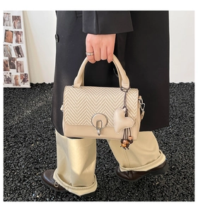 Detail of beige crossbody bag featuring textured weave flap and heart bead charm