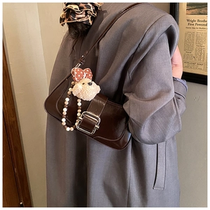Detail of dark brown patent leather underarm bag with silver buckle and plush bear charm