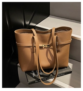 Brown litchi grain tote bag with gold buckle on grey steps next to a book