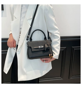 Detail of black contrast handbag with herringbone flap and silver twist lock on white suit