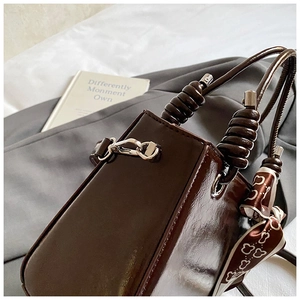 Detail of dark brown patent leather bucket bag with silk scarf and silver metal buckle