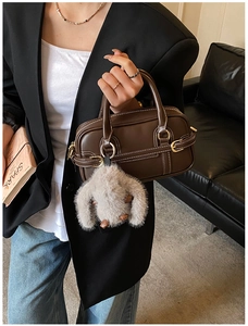 Detailed close-up of brown Boston bag with contrast white stitching and plush bunny charm