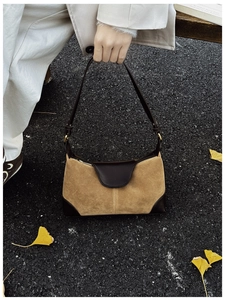 Close-up of suede and leather shoulder bag held against autumn ginkgo leaves background