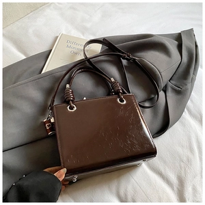 Close-up of vintage brown glossy patent leather handbag with knotted handle and metal studs