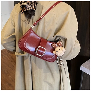 Detail of burgundy patent leather underarm bag with silver buckle and bear charm
