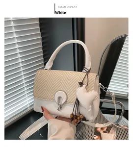 Detail of white leather and straw crossbody bag with metal ring closure and heart charm