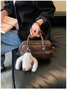 Detail of dark brown Boston bag with white stitching and cute plush rabbit charm