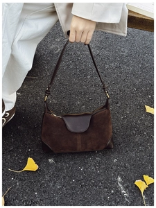 Close-up of brown suede and leather shoulder bag with ginkgo leaves on the ground