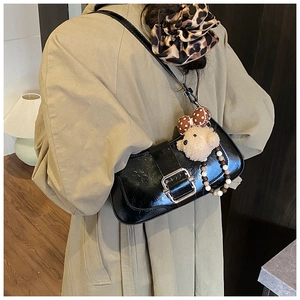 Detail of black glossy baguette bag with silver buckle and plush bear charm on model