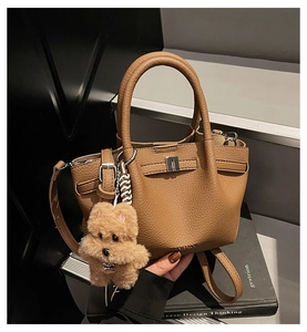 Détail d'un sac seau en cuir marron à motif litchi avec boucle argentée et breloque ours