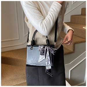 Detail of black patent leather bucket bag with braided handle and patterned silk scarf