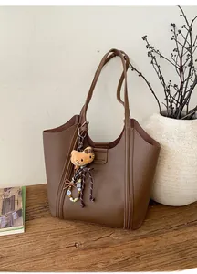 Détail d'un sac cabas marron en cuir texturé avec un pendentif chat sur un bureau en bois