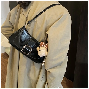 Detail of black patent leather baguette bag with silver buckle and plush bear charm