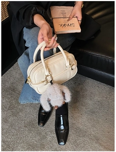 Detail of a beige handbag featuring top handles, zipper and a plush bunny charm decor