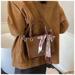 Detail of dark brown patent leather bucket bag with silk scarf and spiral handle detail