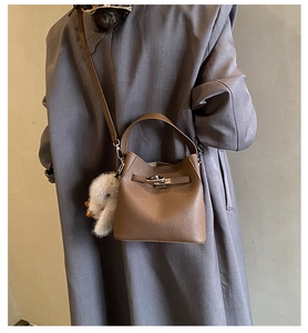 Brown lychee leather bucket bag styled with a gray coat and plush white charm