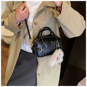 Close-up of a black Boston bag featuring white contrast stitching and cute plush rabbit charm