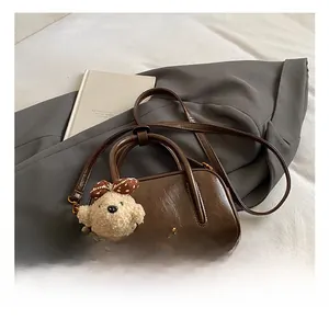 Détail d'un sac Boston marron foncé brillant avec breloque ours et bandoulière réglable