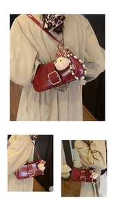 Detail of burgundy glossy leather baguette bag with gold buckle and bear charm