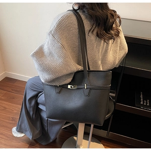 Detail of black pebbled leather tote bag with metallic buckle shown in a modern home setting