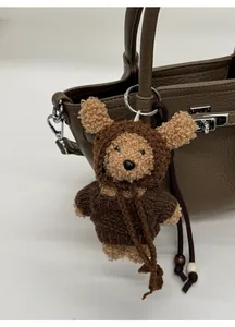 Detail of a plush teddy bear charm with a knitted sweater on a leather bucket handbag