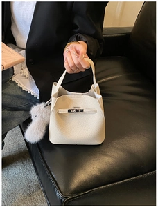 Close-up of beige lychee grain leather bucket bag with silver buckle and plush ball