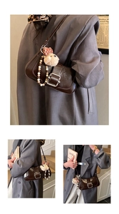 Detail view of dark brown glossy leather shoulder bag with vintage buckle and bear charm