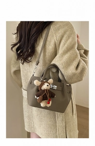 Detail of taupe pebbled leather bucket bag with silver twist lock and plush bear charm