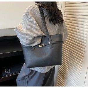Detail view of black lychee grain leather tote bag with gold buckle on casual outfit