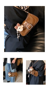 Detailed view of dark brown leather underarm bag with large metal buckle and plush bear charm