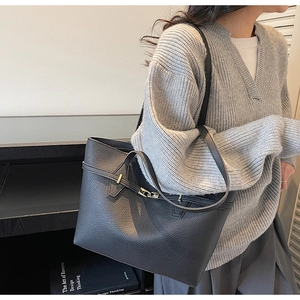 Detail of black pebbled leather tote bag with metallic buckle shown on a model