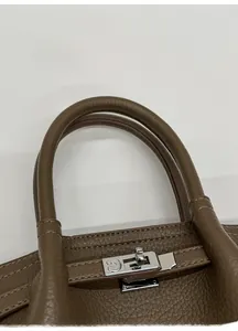 Close-up of litchi grain leather bag with silver metal lock and comfortable handles