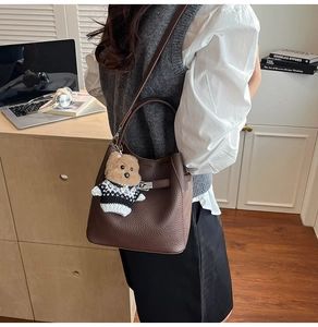 Detail of dark brown litchi grain leather bucket bag with a cute teddy bear charm