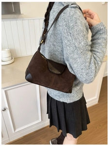 Close-up of brown suede shoulder bag with leather accents on model in casual knitwear