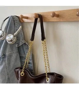 Detail of a dark brown leather tote bag with a bold gold chain strap on a wooden hook