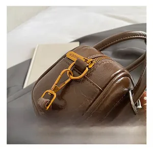 Détail du sac cylindre en cuir marron foncé avec ferrures dorées et breloque en perles