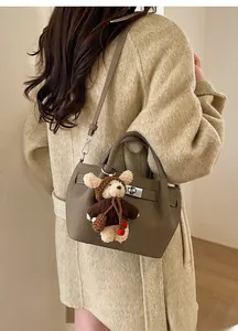 Detail of taupe pebbled leather bucket bag featuring a cute bear plush charm and metal clasp