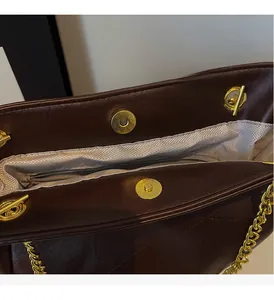 Detail of burgundy quilted leather tote bag featuring gold chain and magnetic snap closure