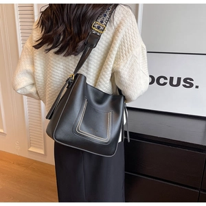 Détail du sac seau en cuir noir avec bandoulière tissée et boucles métalliques dorées
