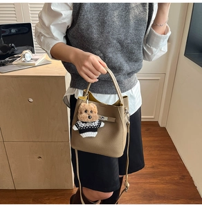 Detail of camel lychee leather bucket bag featuring a secure buckle and plush dog charm