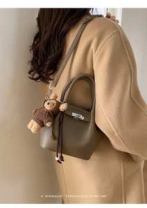 Detail of dark khaki litchi grain leather bucket bag with lock and cute bear charm