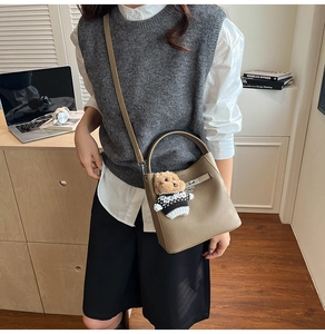 Detail of tan litchi pattern bucket bag with cute teddy bear charm on wooden table