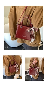 Detail of dark red glossy bucket bag with branded logo and decorative bear pattern silk scarf