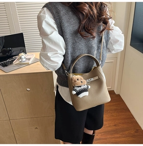 Detailed view of the brown leather bucket bag with silver buckle and plush bear pendant
