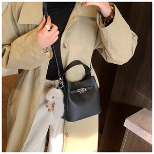 Close-up of black litchi grain leather bucket bag with silver buckle and plush rabbit charm