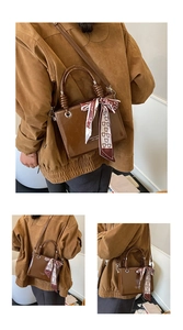 Detail of a brown patent leather crossbody bag featuring a decorative bear print scarf
