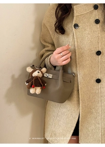 Detail of a khaki leather bucket bag with a plush bear charm and silver twist lock
