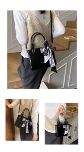 Detail of black glossy bucket bag featuring JITTANO logo and decorative silk scarf