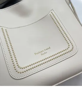 Détail du sac cabas blanc cassé avec logo doré et texture de surpiqûres à rivets